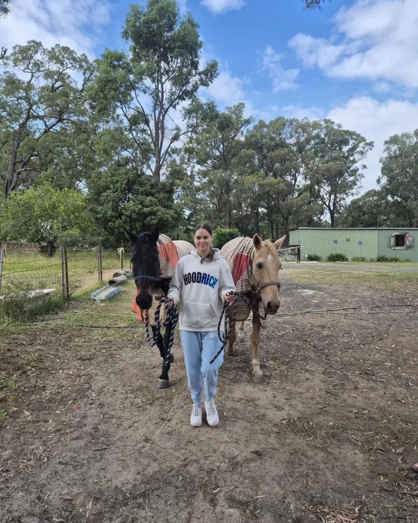 A girl leading two horses across a paddock